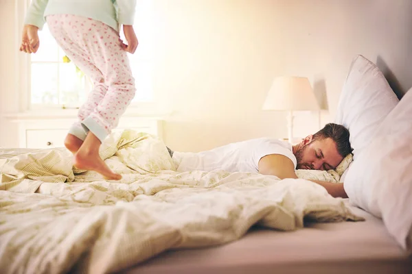 Um pai nunca descansa. Tiro de uma menina alegre pulando na cama para acordar seu pai adormecido em casa. — Fotografia de Stock