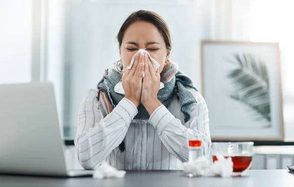 2020, dem Jahr, in dem die Welt krankgeschrieben wurde. Aufnahme einer jungen Geschäftsfrau, die sich an ihrem Schreibtisch in einem modernen Büro die Nase pustet. — Stockfoto