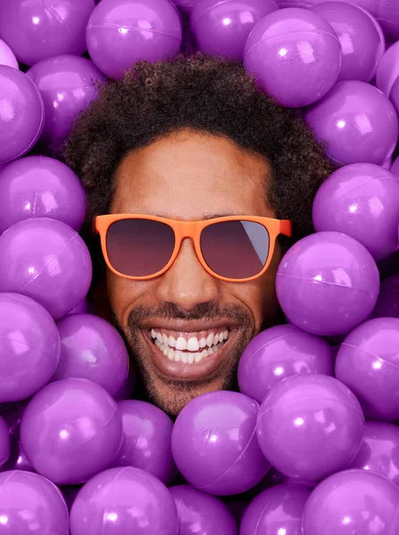 Du ser cool och galen ut. En ung svart man ansikte bland lila grop bollar. — Stockfoto