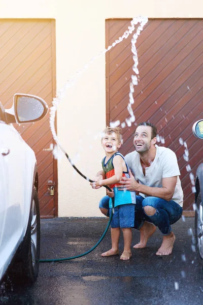 Se están divirtiendo mucho. Largura completa de un padre y un hijo jugando con una manguera mientras se lava un coche juntos. — Foto de Stock