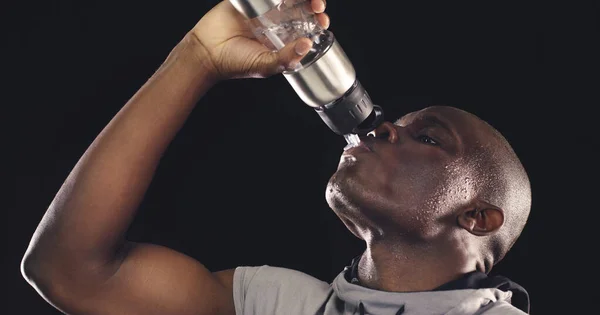 Apagando mi sed antes de hacer mis últimas repeticiones. Estudio de un joven deportista bebiendo de una botella de agua sobre un fondo oscuro. — Foto de Stock
