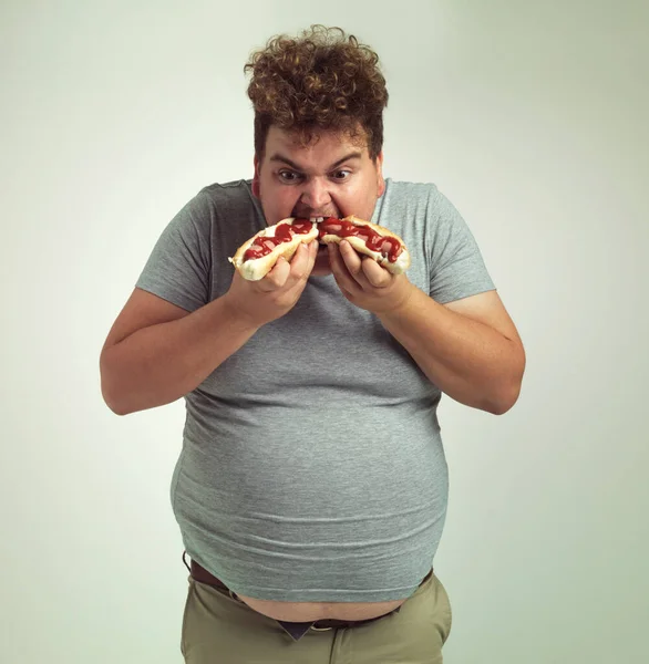 I cant get enough of these hotdogs. Studio shot of an overweight man eating two hotdogs at once. — Stock Photo, Image