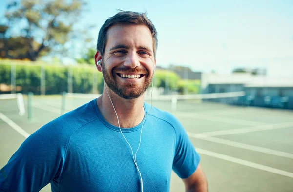 Ως αθλητής, η φυσική κατάσταση έρχεται πάντα πρώτη. Πορτρέτο ενός αθλητικού νεαρού άνδρα που ακούει μουσική ενώ γυμνάζεται σε γήπεδο τένις. — Φωτογραφία Αρχείου