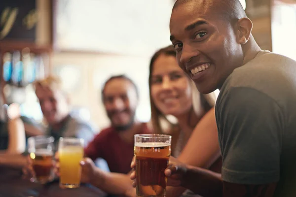 Blij dat je kon komen. Portret van een lachende jongeman in een bar met wat vrienden. — Stockfoto