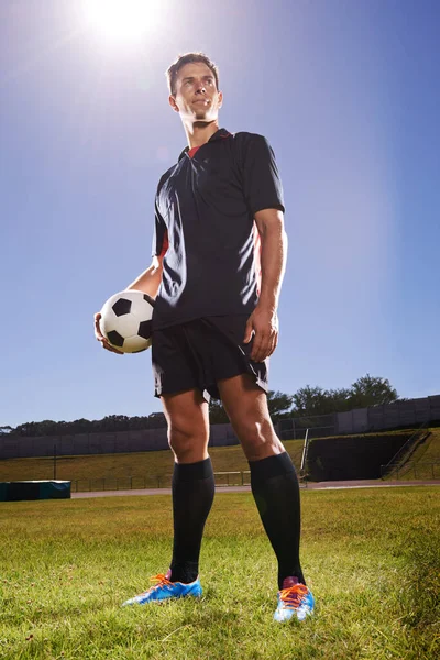 Hrdina her. Zastřelen mladým fotbalistou stojícím na hřišti s míčem v rukou. — Stock fotografie
