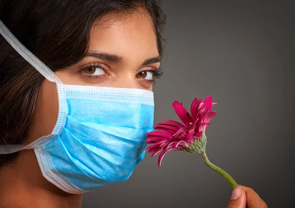 Não consigo cheirar nada. Close-up de uma jovem mulher com uma máscara de médicos em olhar para a câmera e cheirar uma flor. — Fotografia de Stock