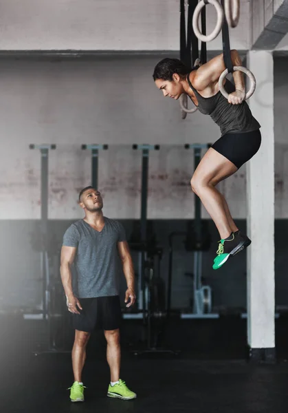 Натискання свого учня на вищі рівні. Повнометражний знімок молодої жінки, яка працює над гімнастичними кільцями, поки її тренер дивиться на . — стокове фото