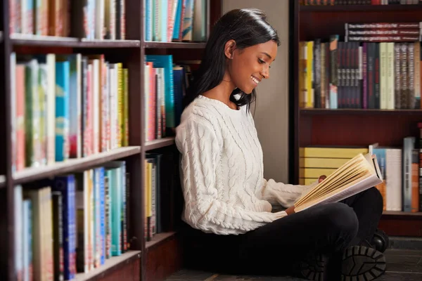 Questo è un capitolo piuttosto eccitante. Girato di una giovane donna che legge un libro seduta sul pavimento contro una libreria in una biblioteca. — Foto Stock