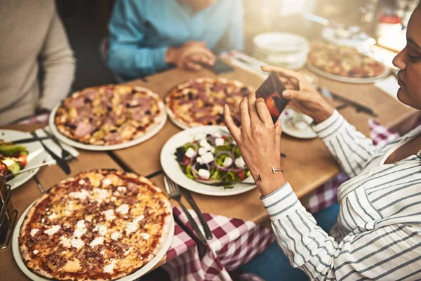 Pizza. Tiro de um grupo de pessoas sentadas em uma mesa com pratos de pizza na frente deles, enquanto se tira uma foto dele dentro de um restaurante. — Fotografia de Stock