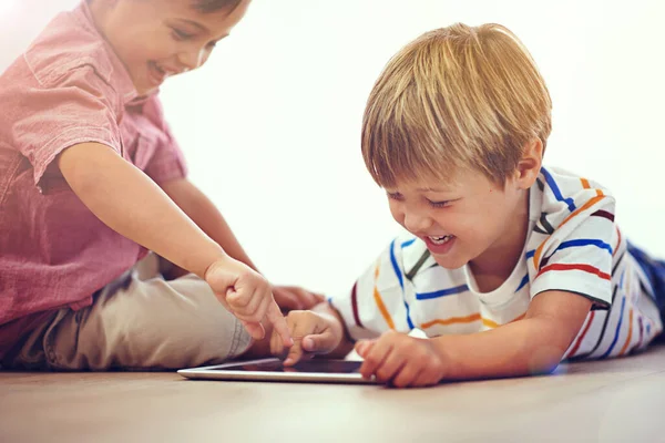 Il s'amuse tellement en ligne. Prise de vue de deux petits garçons utilisant une tablette numérique ensemble tout en étant assis sur le sol. — Photo
