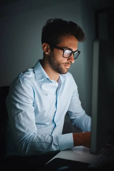 De hele nacht doorgaan om vooruit te komen. Opname van een jonge zakenman die laat werkt op een computer in een kantoor. — Stockfoto