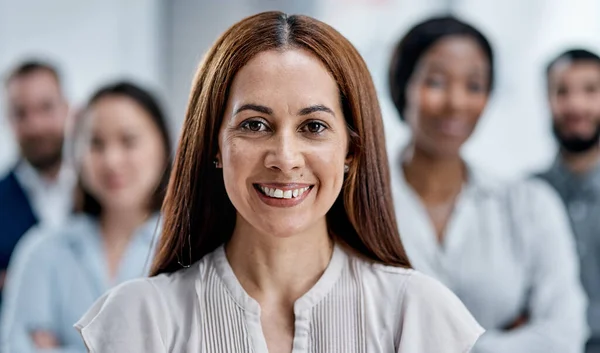 Jag tar mitt team direkt till toppen. Porträtt av en affärskvinna som står på ett kontor med sina kollegor i bakgrunden. — Stockfoto