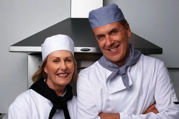 Glimlachende mannelijke en vrouwelijke koks samen in de keuken. Portret van een lachende mannelijke en vrouwelijke chef-koks die samen in de keuken staan. — Stockfoto