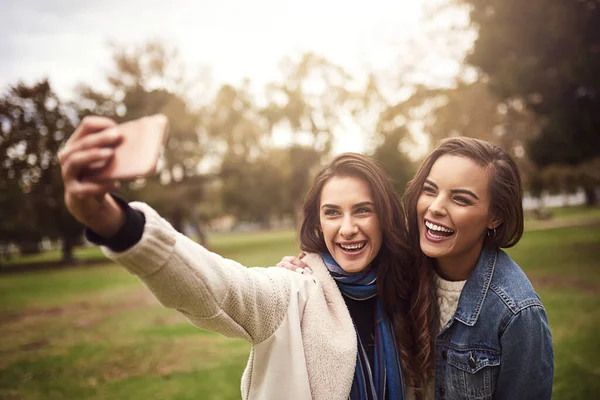 Nos encanta tomarnos selfies juntos. Fotografía de dos alegres jóvenes amigos tomando un autorretrato juntos afuera en un parque. — Foto de Stock