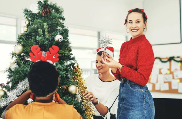 Parlayan yıldız olmadan bir Noel ağacı tamamlanmış sayılmaz. Çekici genç bir iş kadınının, iş arkadaşlarıyla Noel ağacı süslemesi.. — Stok fotoğraf