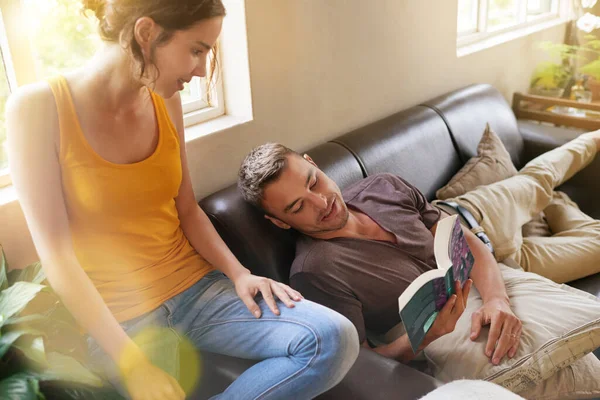 Es como si el autor escribiera nuestra historia de amor personal. Fotografía de un joven leyendo un libro mientras se relaja en el sofá con su esposa. — Foto de Stock