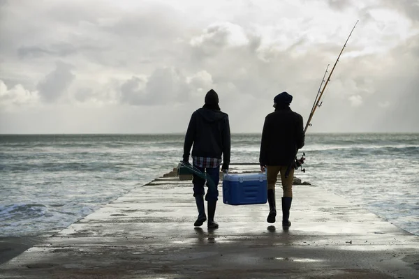 Carrying home their catch. Shot of two young men fishing at the ocean in the early morning. — ストック写真