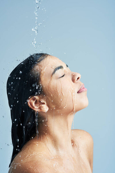 Long shower after a long day. Shot of a young woman having a shower against a blue background.