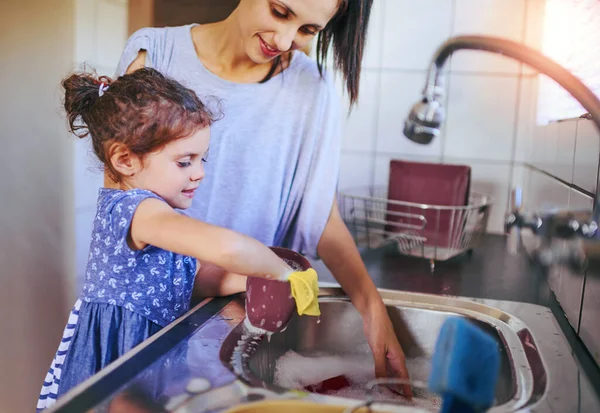A házimunka sokkal szórakoztatóbb, ha együtt csináljuk. Egy boldog kislányról és az anyjáról, akik együtt mosogatnak otthon.. — Stock Fotó