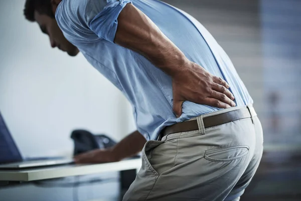 Its so painful I cant even stand up properly. Shot of a young businessman suffering with back pain at work. — Stock Photo, Image