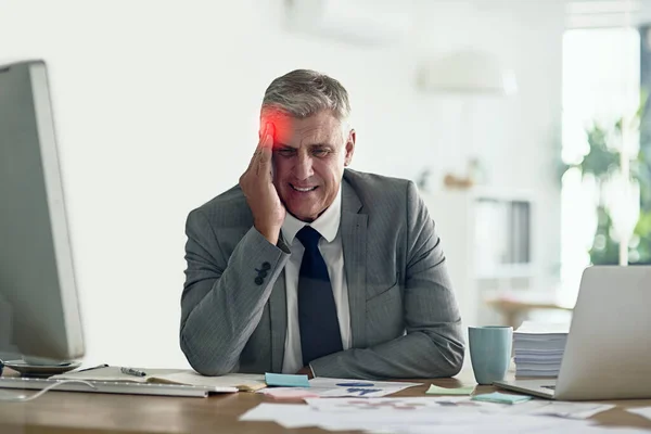 Diriger une entreprise peut être très pénible. Tir d'un homme d'affaires avec un mal de tête tenant la tête alors qu'il était assis à son bureau. — Photo