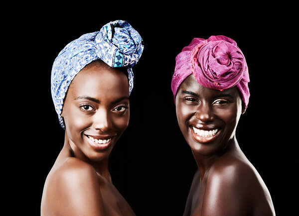 Studio portrait of two beautiful women wearing headscarves against a black background.
