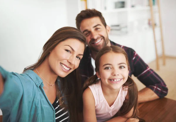 Ta rodzina nie jest nieśmiała. Portret szczęśliwej pary małżeńskiej i ich młodej córki pozujących do selfie razem w domu. — Zdjęcie stockowe