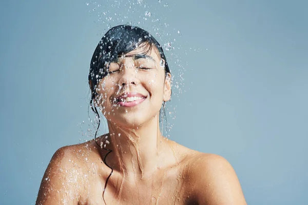 Csodálatosan újjáéleszti a vizet. Lövés egy fiatal nőről, aki frissítő zuhanyt tart a kék háttér előtt. — Stock Fotó