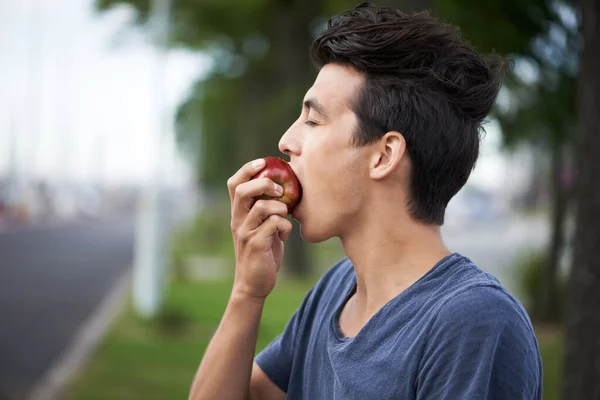 Taking a bite. A young man taking a bite of an apple while waiting for the bus. — ストック写真