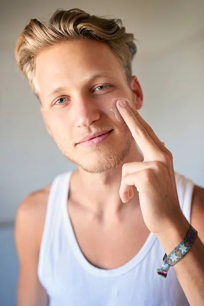 Halten Sie Ihre Haut mit Feuchtigkeit versorgt. Schnappschuss eines jungen Mannes, der ihm Feuchtigkeitscreme ins Gesicht sprüht. — Stockfoto