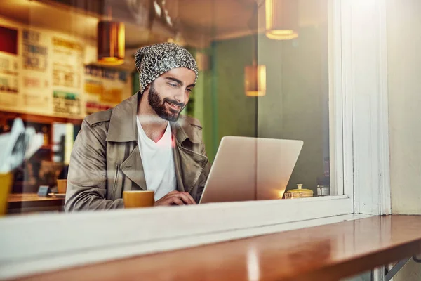 A entrar online no café dele. Tiro de um jovem bonito sentado em um balcão de café usando um laptop. — Fotografia de Stock