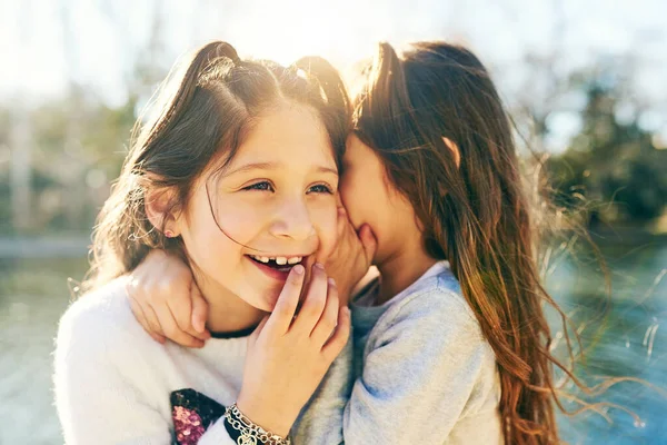 Partager des secrets avec ma sœur. Plan recadré d'une adorable petite fille chuchotant dans l'oreille de ses sœurs à l'extérieur. — Photo