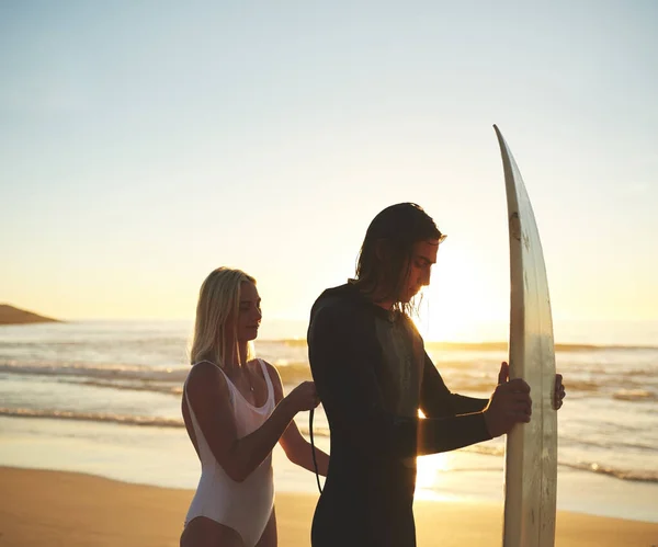 Pronto para montar algumas ondas. Tiro recortado de um jovem casal a fechar o fato de mergulho antes de surfar ao pôr-do-sol. — Fotografia de Stock