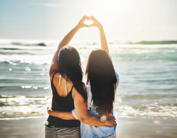 Kami berbagi cinta untuk hal-hal yang indah. Rearview shot of two friends formed a heart shape together on the beach. — Stok Foto
