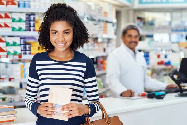 My local pharmacy stocks all that I need. Portrait of a young woman standing in a chemist with a pharmacist in the background. — Stock Photo, Image