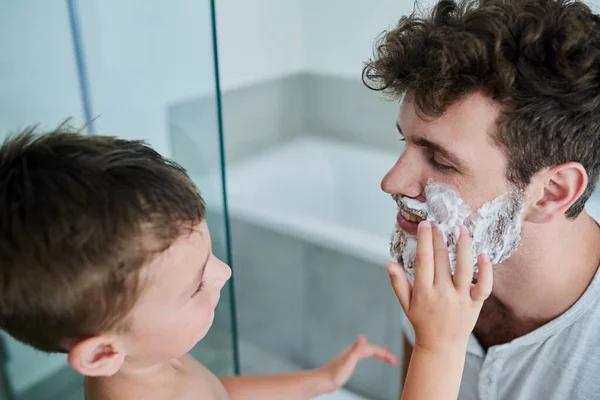 Let me do it for you Dad. Shot of a little boy rubbing shaving cream on his fathers face in the bathroom at home. — Stock Photo, Image