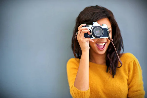 Felice furbo. Studio ritratto di una giovane donna che utilizza una fotocamera vintage su uno sfondo grigio. — Foto Stock