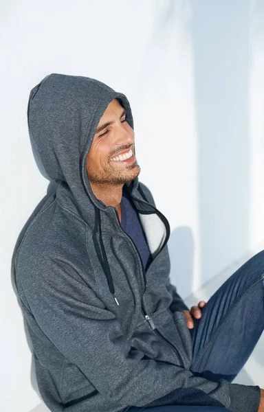 Happy to hangout. A handsome young man sitting on the floor and smiling while wearing a hoodie. —  Fotos de Stock
