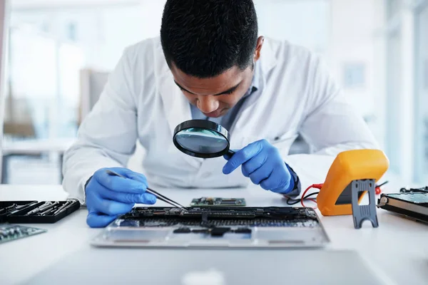 Non lasciare nulla di intentato. Girato di un giovane uomo che usa pinzette e una lente d'ingrandimento mentre ripara l'hardware del computer in un laboratorio. — Foto Stock