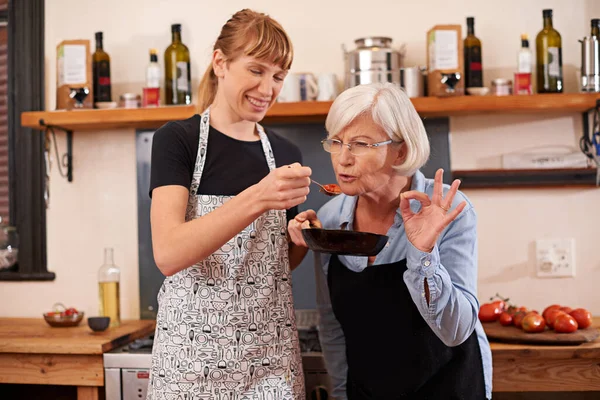 Always taste your food they say. Shot of a senior woman and a younger woman cooking together. — стоковое фото