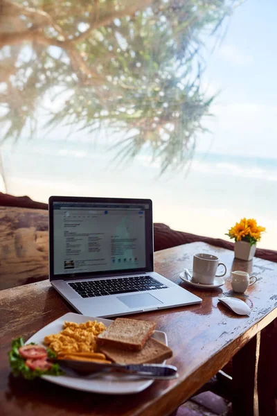 Rise and shine alongside the sea. Shot of a laptop and freshly made breakfast on a table with a view of the beach in the background. — ストック写真