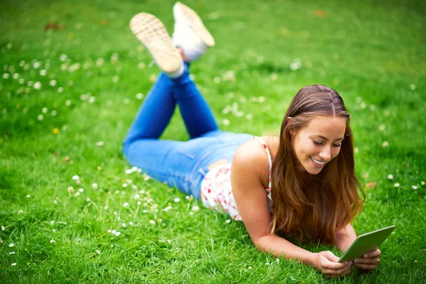 Snubblar på några stora webbplatser. Skjuten av en ung kvinna som använder sin digitala tablett när hon ligger på gräset i parken. — Stockfoto