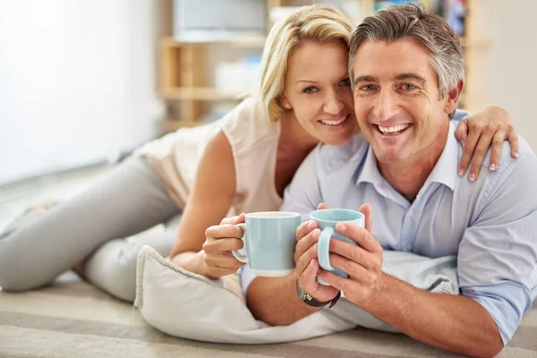 We konden niet gelukkiger zijn. Portret van een glimlachend volwassen paar liggend op hun woonkamer vloer koffie drinken. — Stockfoto