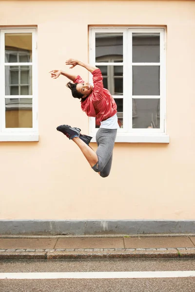 Voller Energie. Eine energische junge Frau in urbaner Sportbekleidung springt auf die Straße. — Stockfoto