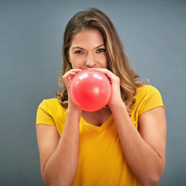 Inflaters gonna inflate. Shot of a young woman inflating a balloon against a gray background. — ストック写真