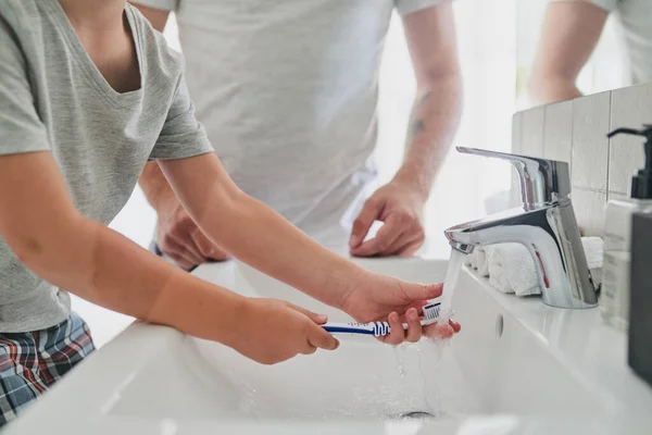 Os bons hábitos começam todas as manhãs. Foto de perto de um menino irreconhecível escovando os dentes com seu pai na casa de banho em casa. — Fotografia de Stock