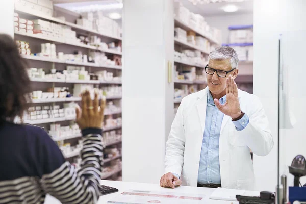 Legyen szép napjuk. Egy vidám, érett férfi gyógyszerész fotózása, aki a gyógyszertárban üdvözöl egy vásárlót.. — Stock Fotó