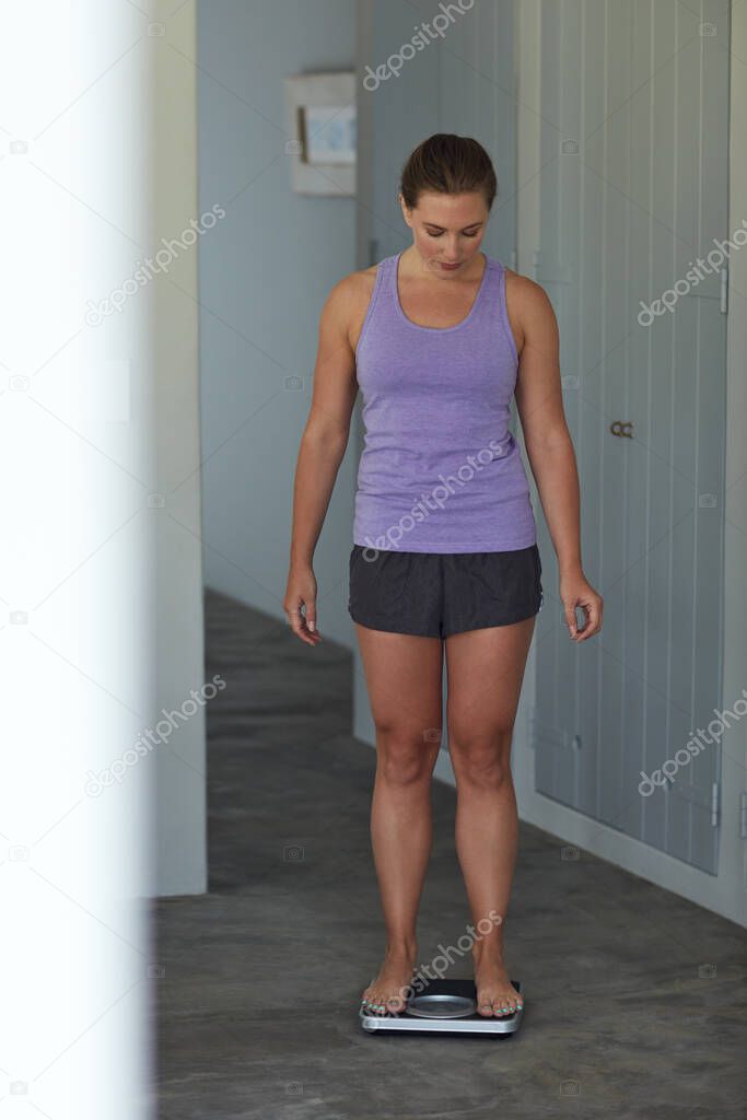 Time to see if her hard work paid off. Shot of a young attractive woman weighing herself on a scale at home.