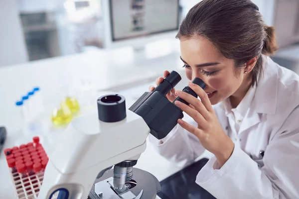 Nie widzę żadnych różnic w tym eksperymencie. Ujęcie wesołej młodej kobiety naukowca patrzącej przez obiektyw mikroskopu, siedzącej w laboratorium.. — Zdjęcie stockowe