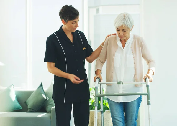 Stai andando alla grande. Colpo ritagliato di un attraente giovane operatore sanitario che aiuta il suo paziente anziano a camminare con un deambulatore in una casa di cura. — Foto Stock
